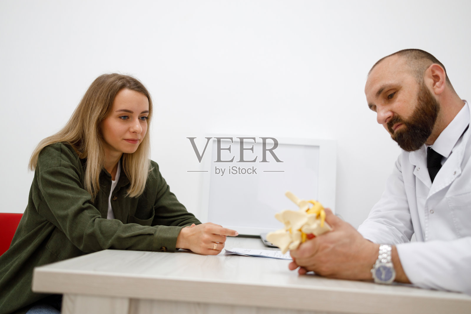 男外科医生向女患者展示腰椎间盘模型上的椎间疝。女人在看医生照片摄影图片