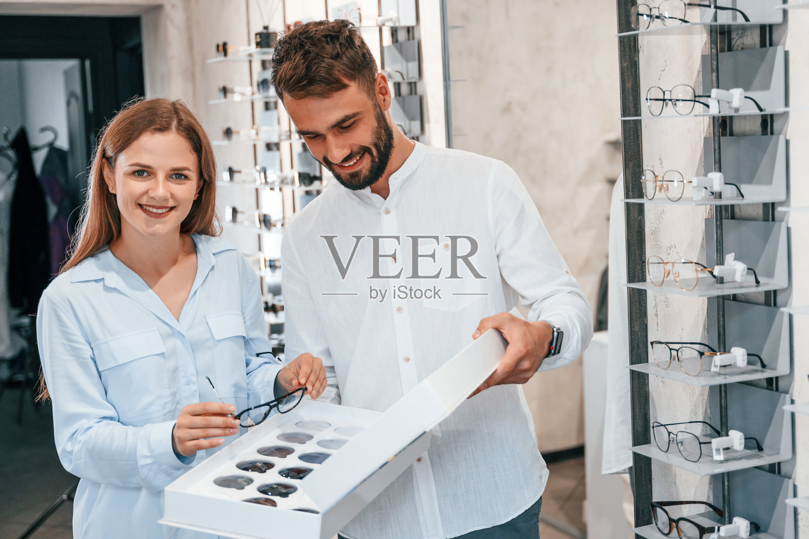 站和微笑。眼镜店里的一对男女。帮助选择产品照片摄影图片