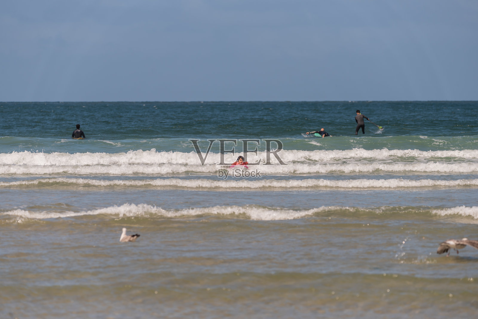 在阿威罗海滩的海浪中,男孩带着橙色的设备和冲浪板练习照片摄影图片