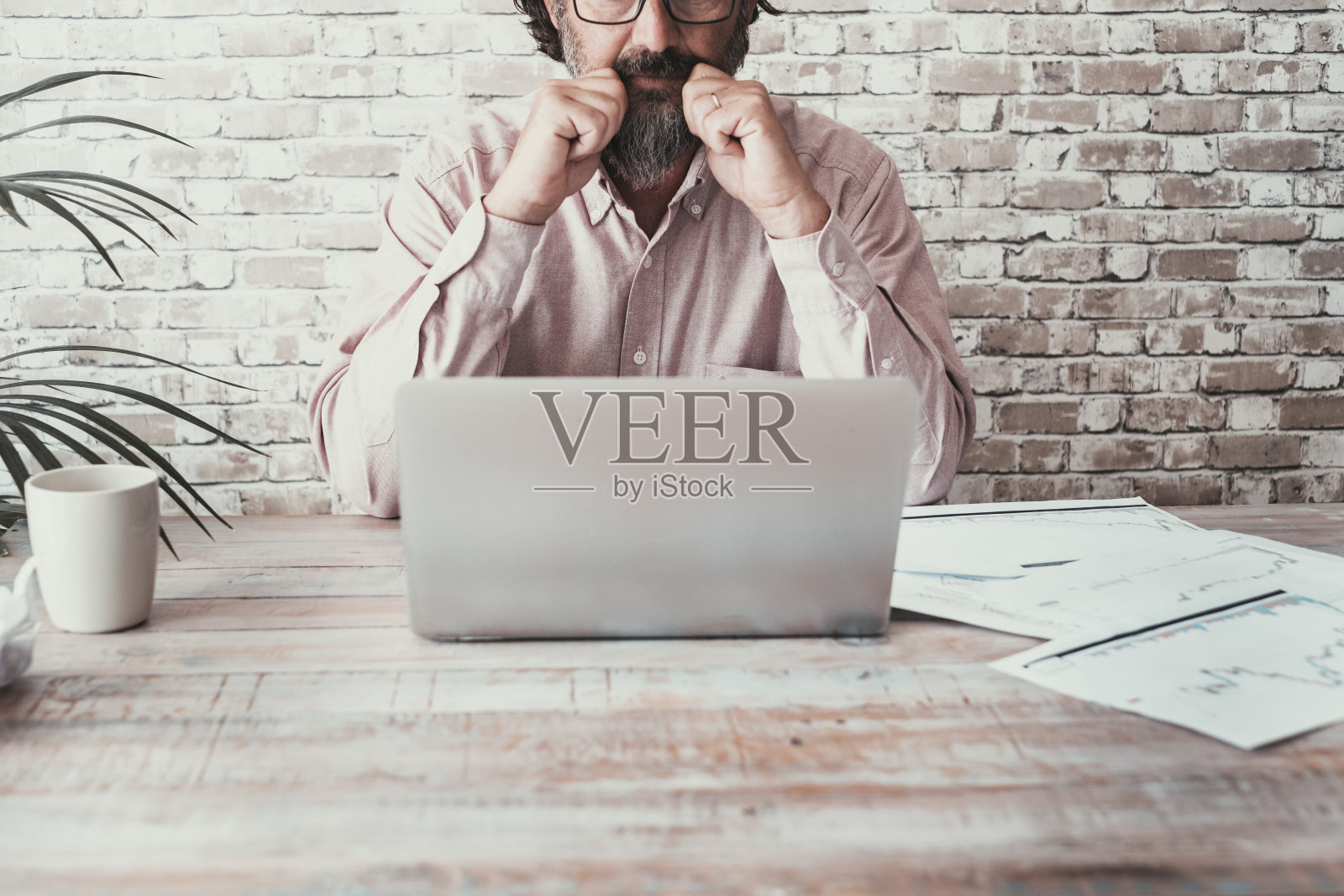 前视图的人在桌子上工作与笔记本电脑和纸图表。业务和工作活动的概念。木桌,人用电脑管理公司。一名员工在室内思考照片摄影图片