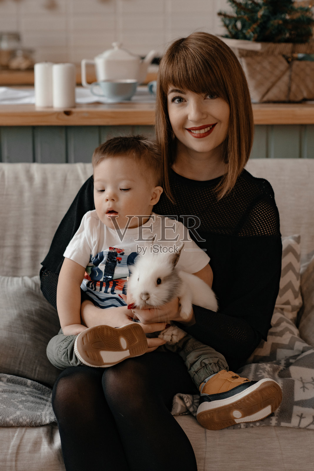 妈妈抱着患有唐氏综合征的儿子坐在沙发上,玩着兔子照片摄影图片