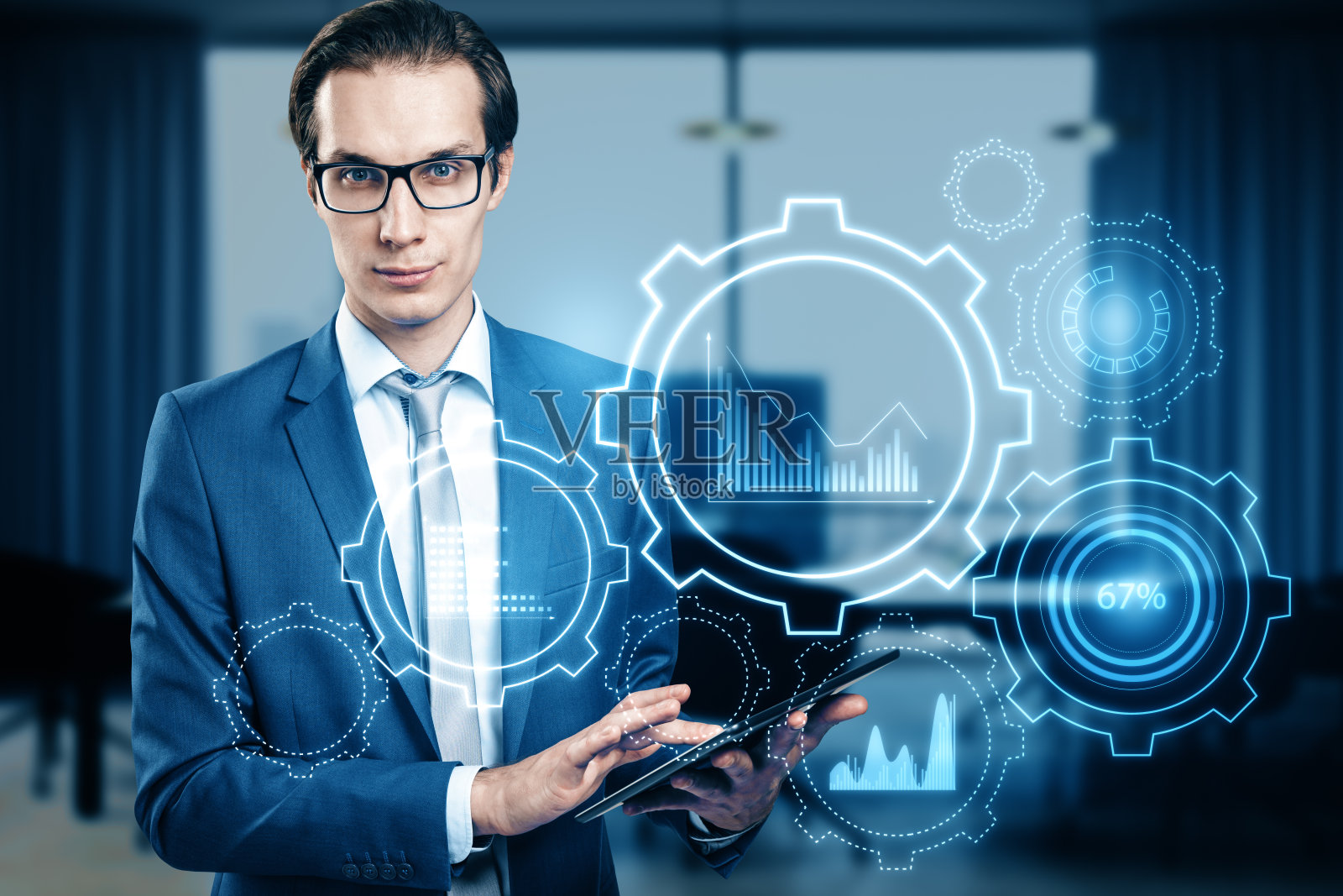 迷人的年轻欧洲商人与数字pad和发光的齿轮和图表全息图在模糊的办公室内部背景。商业分析和财务概念。双重曝光。照片摄影图片