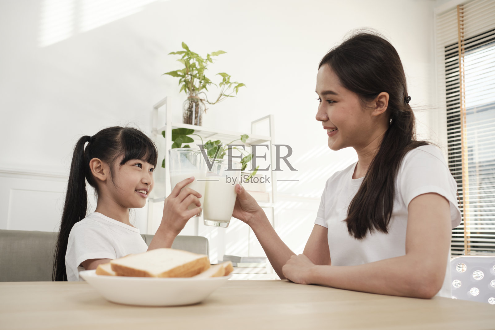 一位健康的亚洲母亲和女儿一起在餐桌上喝新鲜的牛奶。照片摄影图片