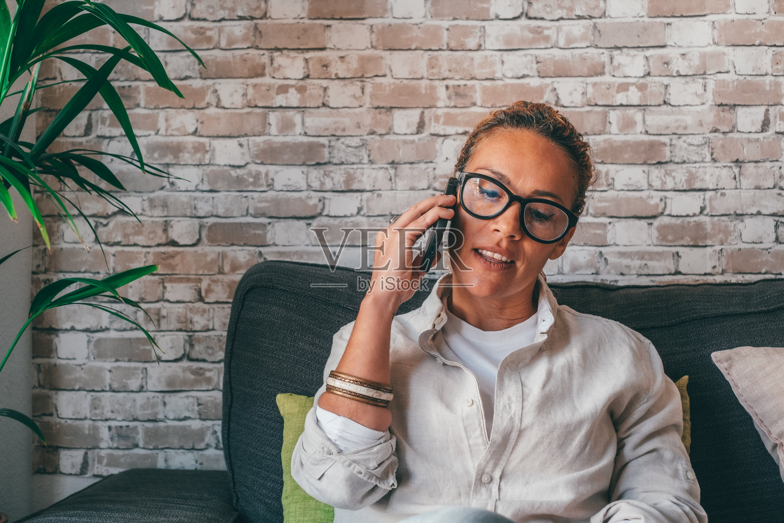微笑的卷发女人在家里打电话,快乐的年轻女孩拿着手机接听电话,迷人的中年与朋友用手机聊天照片摄影图片