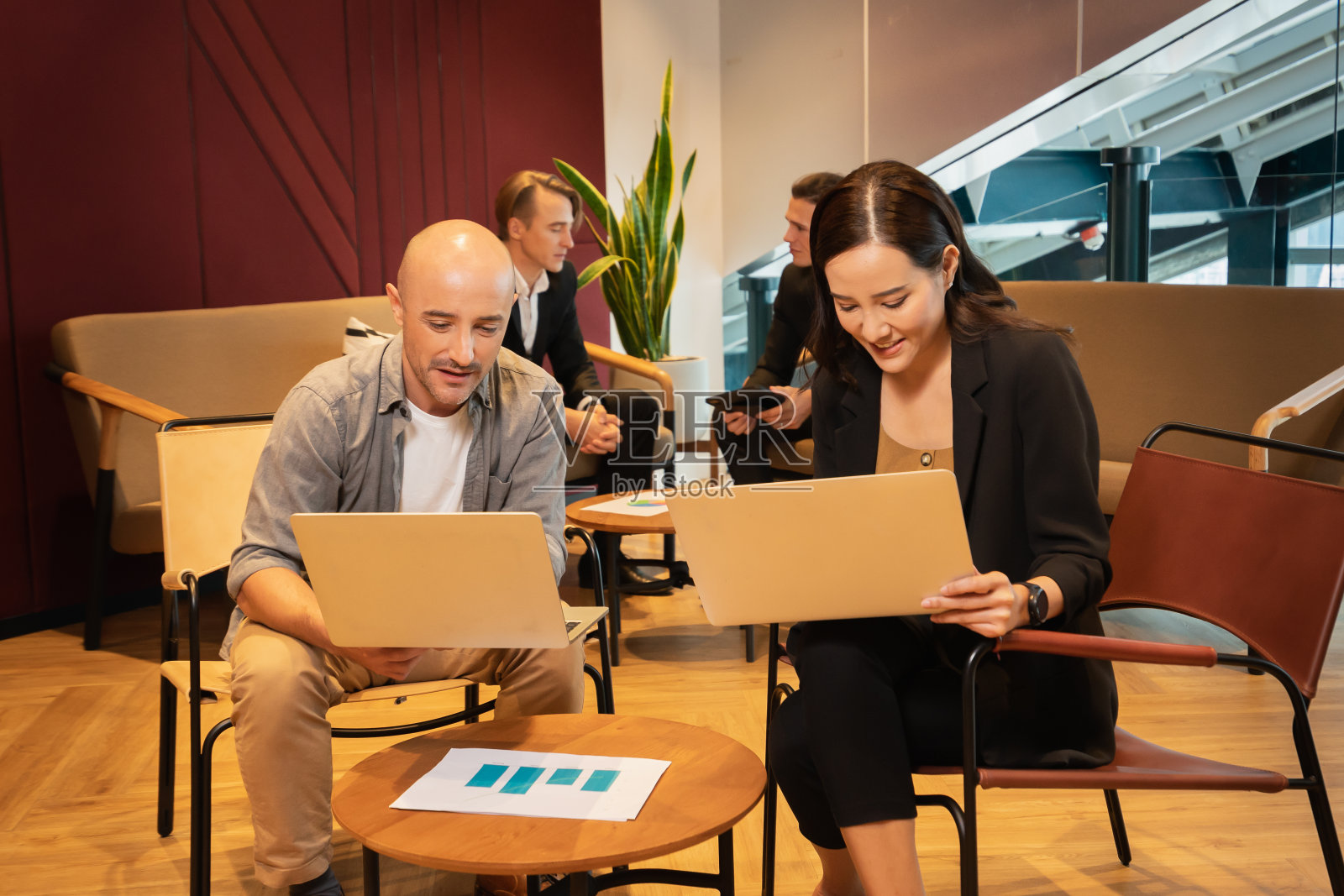 女商人和男伙伴用笔记本电脑一起工作,两个商人在后台讨论。在现代办公室工作的男女同事照片摄影图片