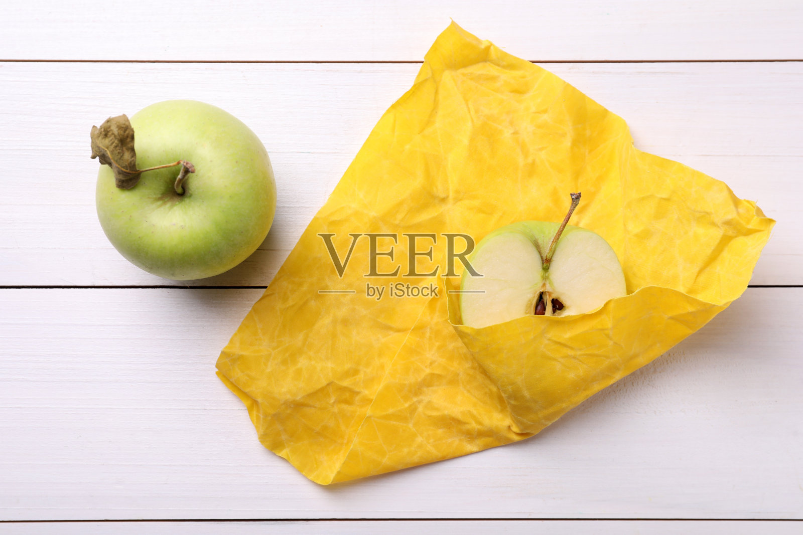 半颗苹果用黄色蜂蜡包裹在白色木桌上,俯视图照片摄影图片