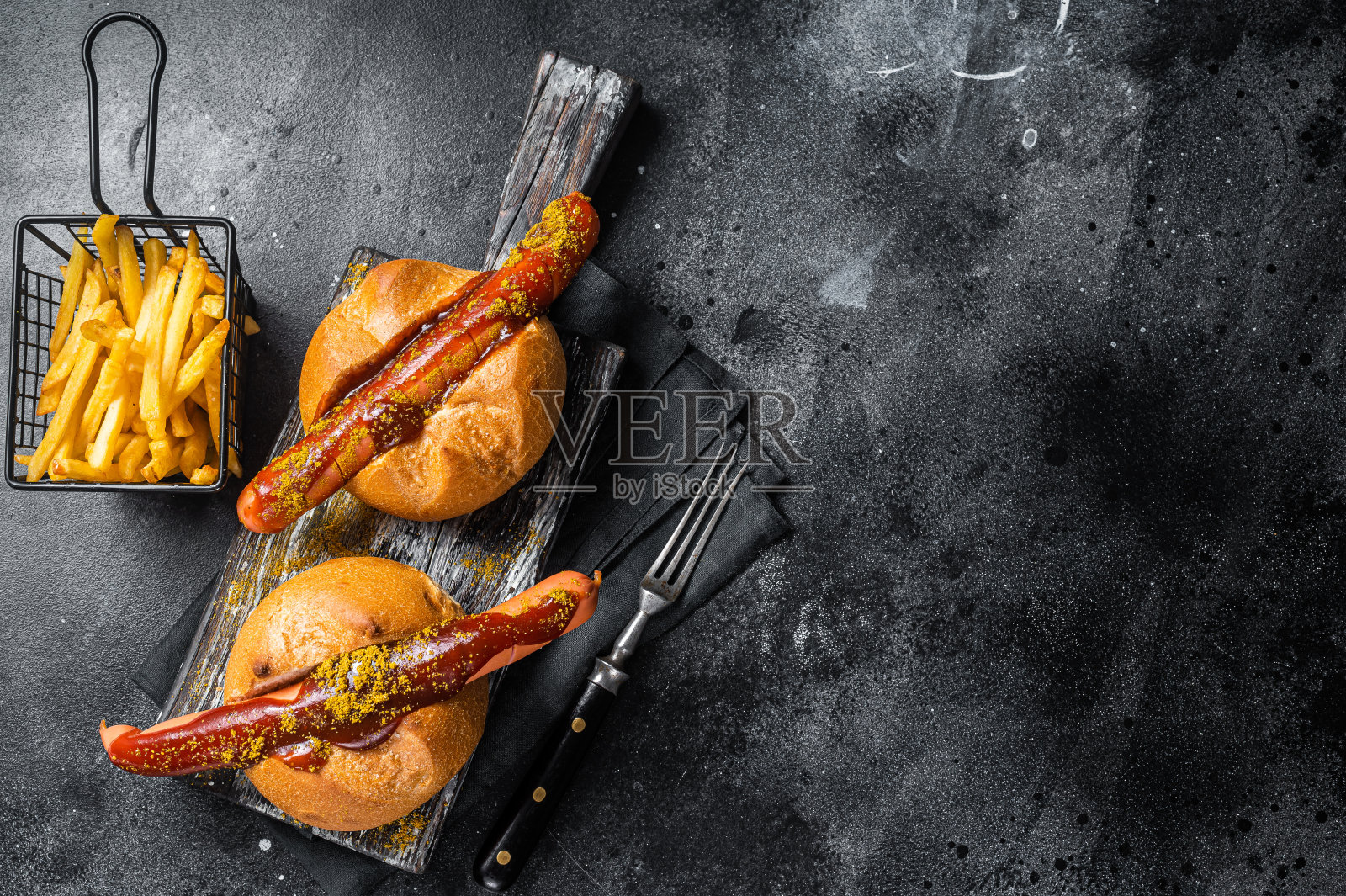 德国香肠夹在小圆面包里配上炸薯条和咖喱酱,咖喱香肠。黑色背景。前视图。本空间照片摄影图片