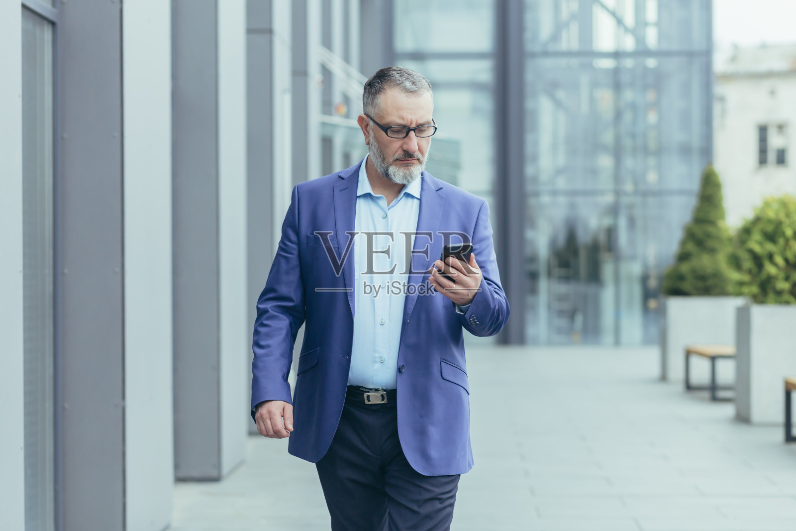 西装革履的商人走在办公中心附近的街道上,拿着手机,正在打字照片摄影图片