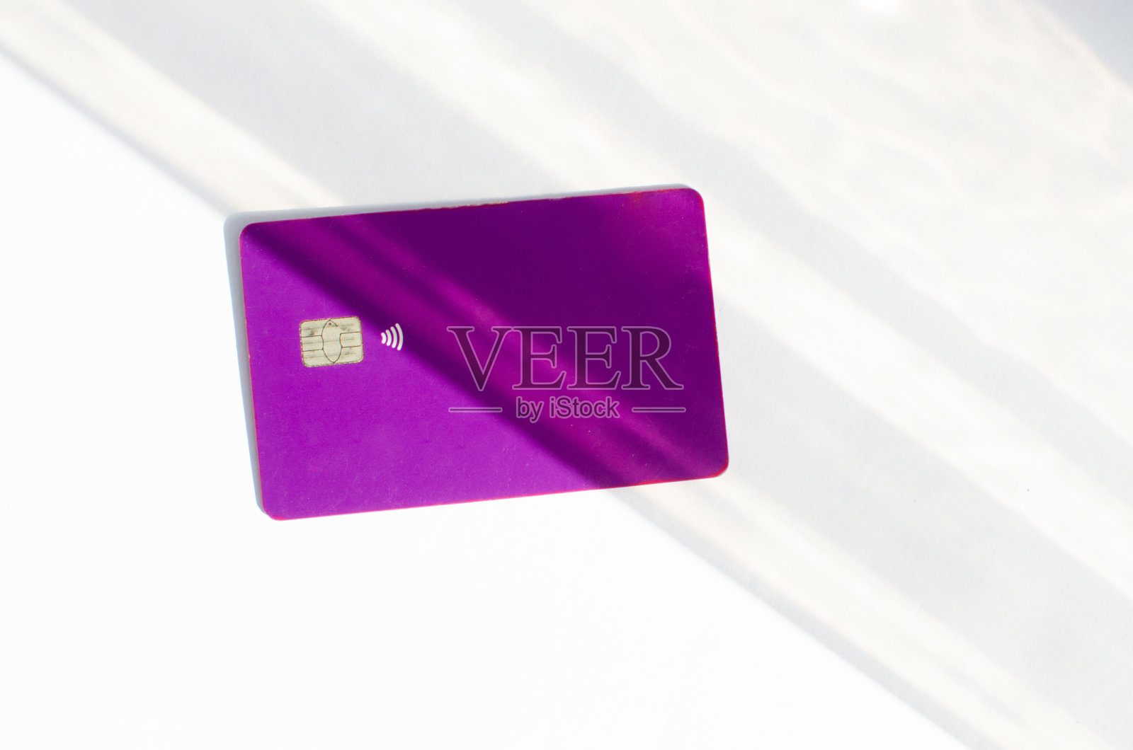 塑料信用卡与芯片可见,在桌上与柔和的灯光和阴影。白色表面的紫色卡片。概念:金融、购买、支付、贷款、支出、投资和债务。照片摄影图片