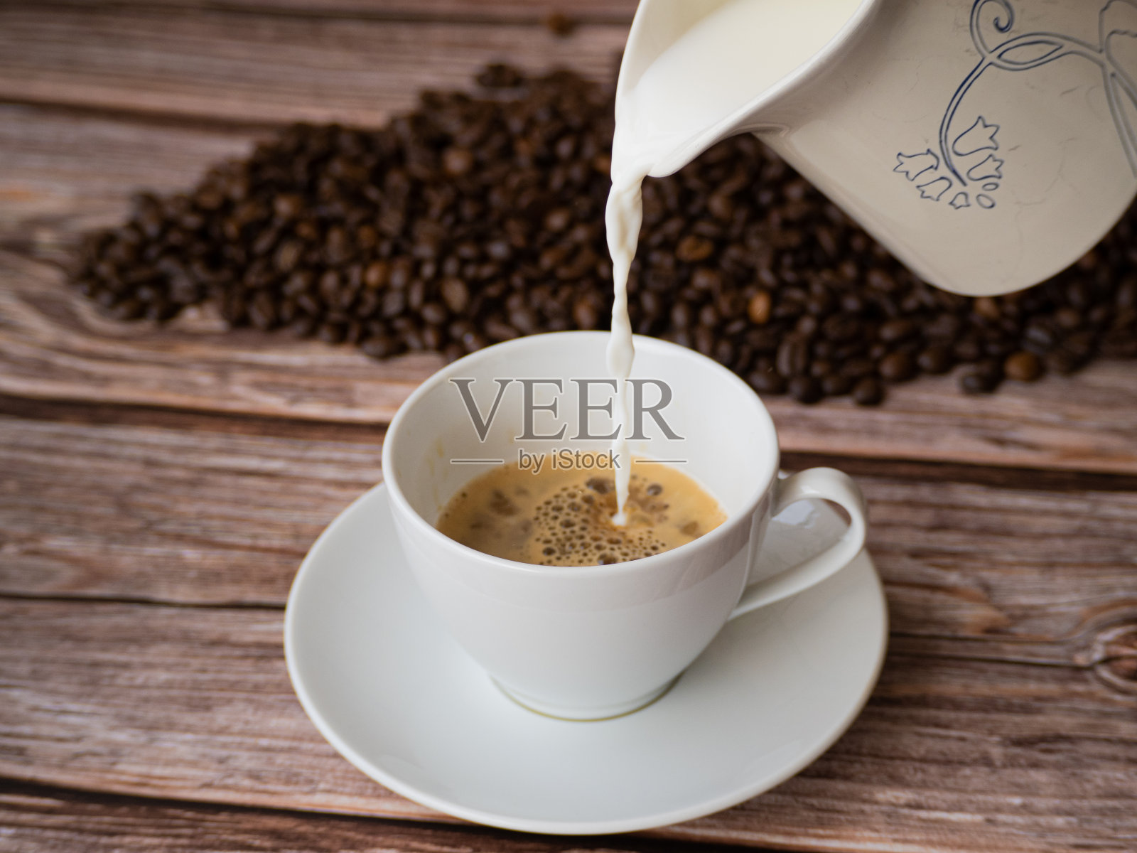 把牛奶倒进一杯白色的咖啡里。照片摄影图片