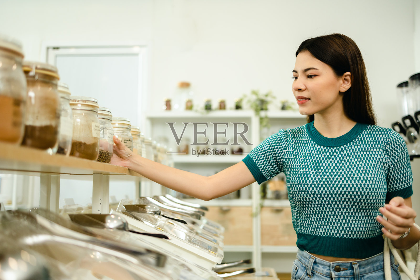 妇女在可持续的无塑料食品杂货店购买谷物和谷物,用可重复使用的袋子补充商店。环保、可持续的生活方式。照片摄影图片