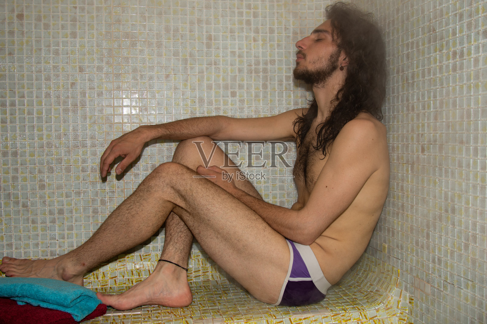 一个留着长发的帅哥正在蒸桑拿。照片摄影图片