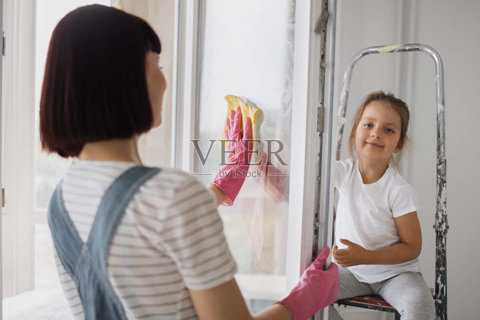 美丽的白人母亲和女儿一起在房间里擦窗户。照片摄影图片