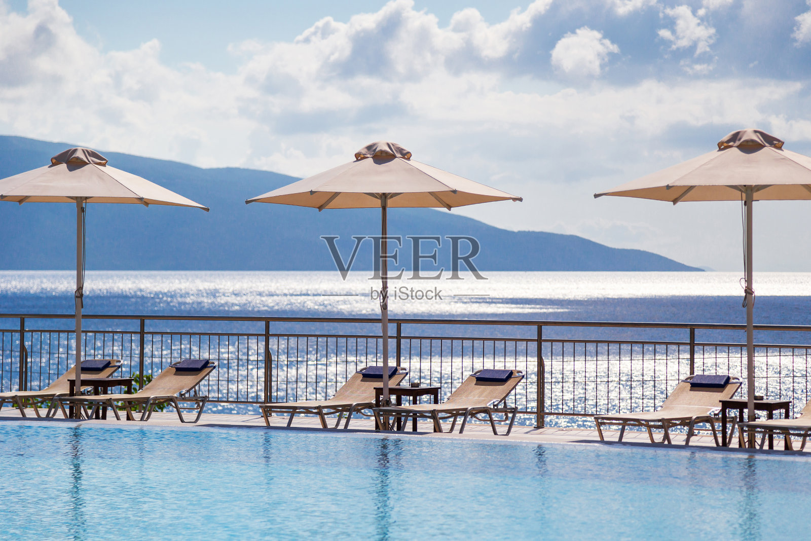 度假村的豪华游泳池,空的躺椅和雨伞与美丽的海景照片摄影图片