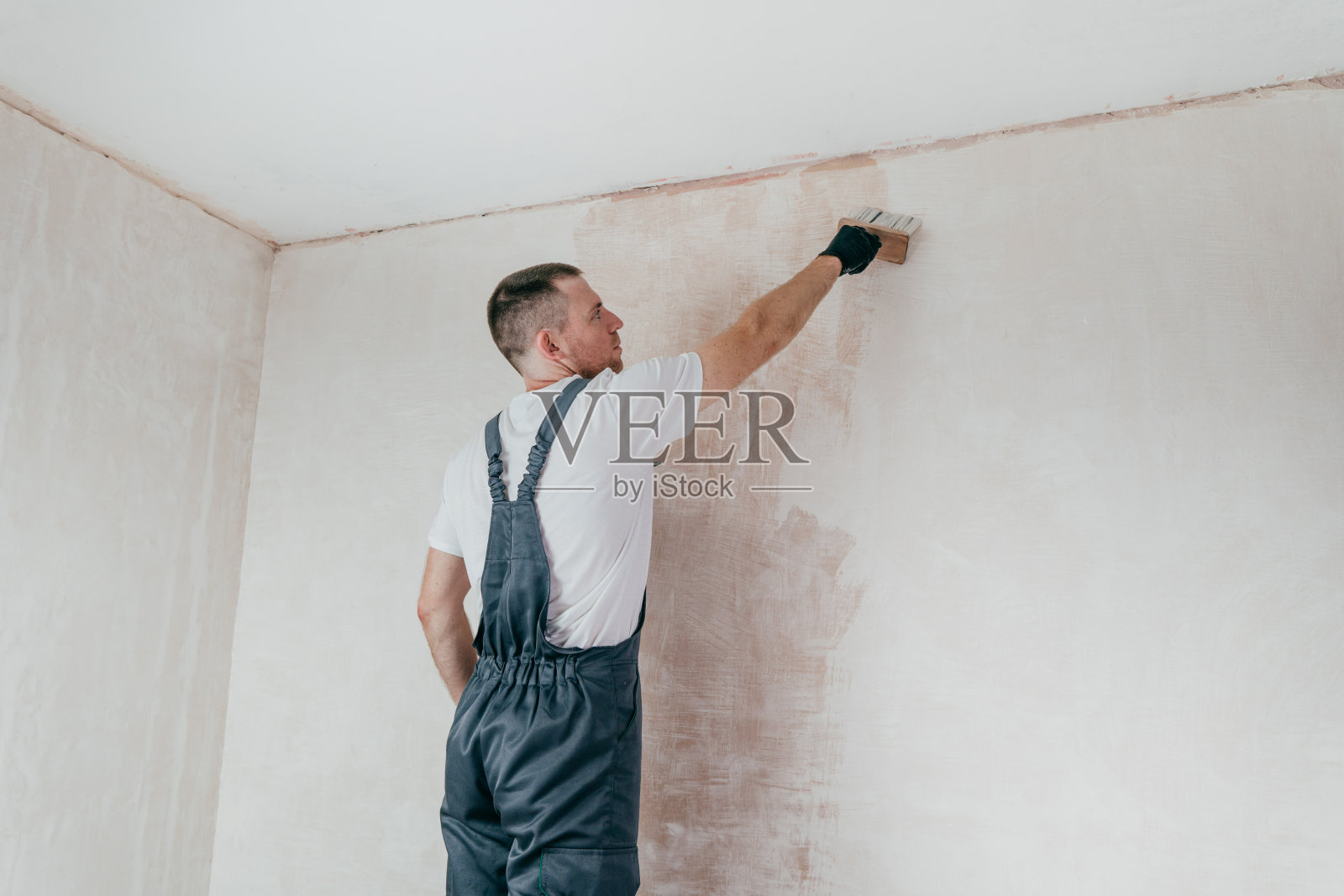穿着工作服的男工人正在用油漆刷涂墙照片摄影图片