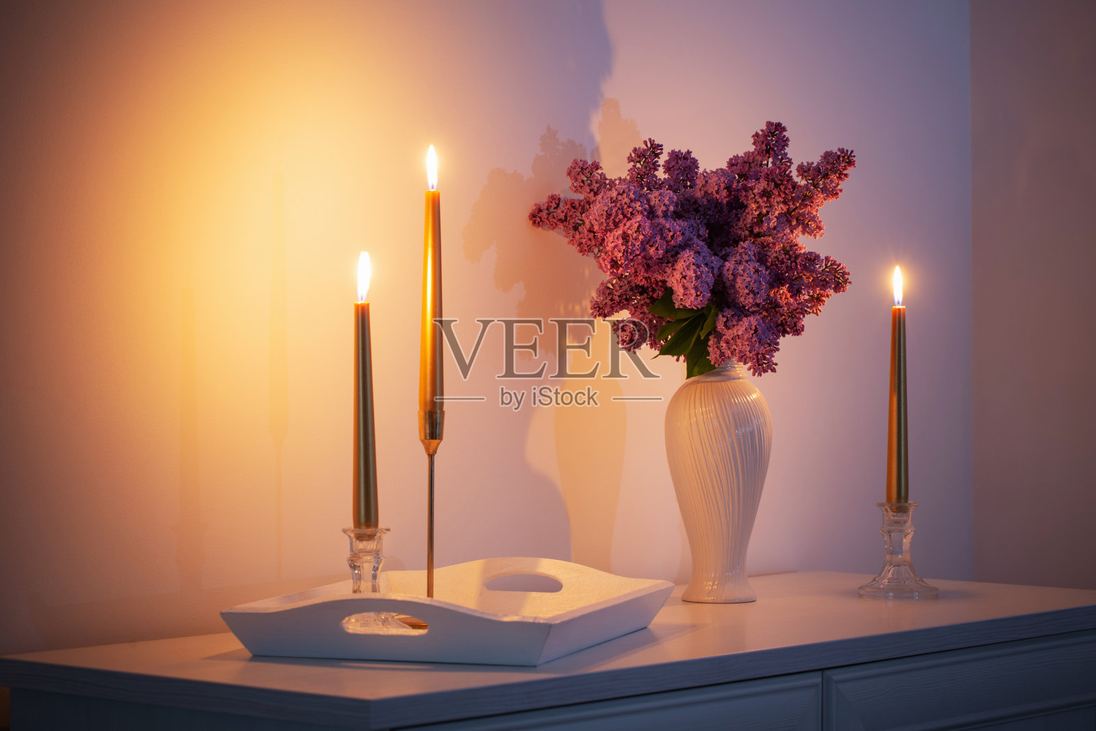 紫丁香花在白色花瓶和金色蜡烛在背景白色墙壁照片摄影图片