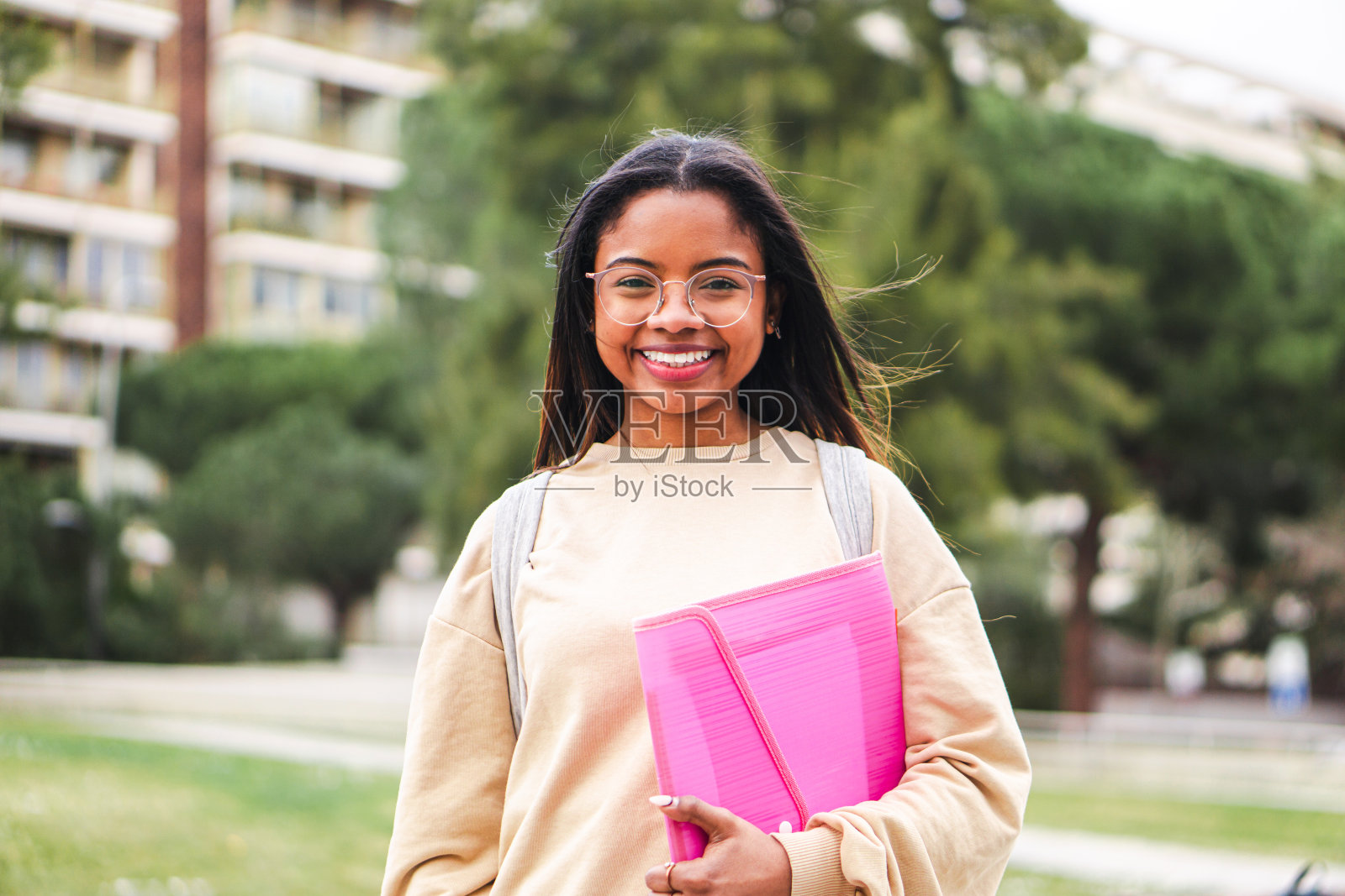 快乐的西班牙女学生戴着眼镜,微笑着笑着走出教室。可爱的青少年学生站在大学校园里照片摄影图片