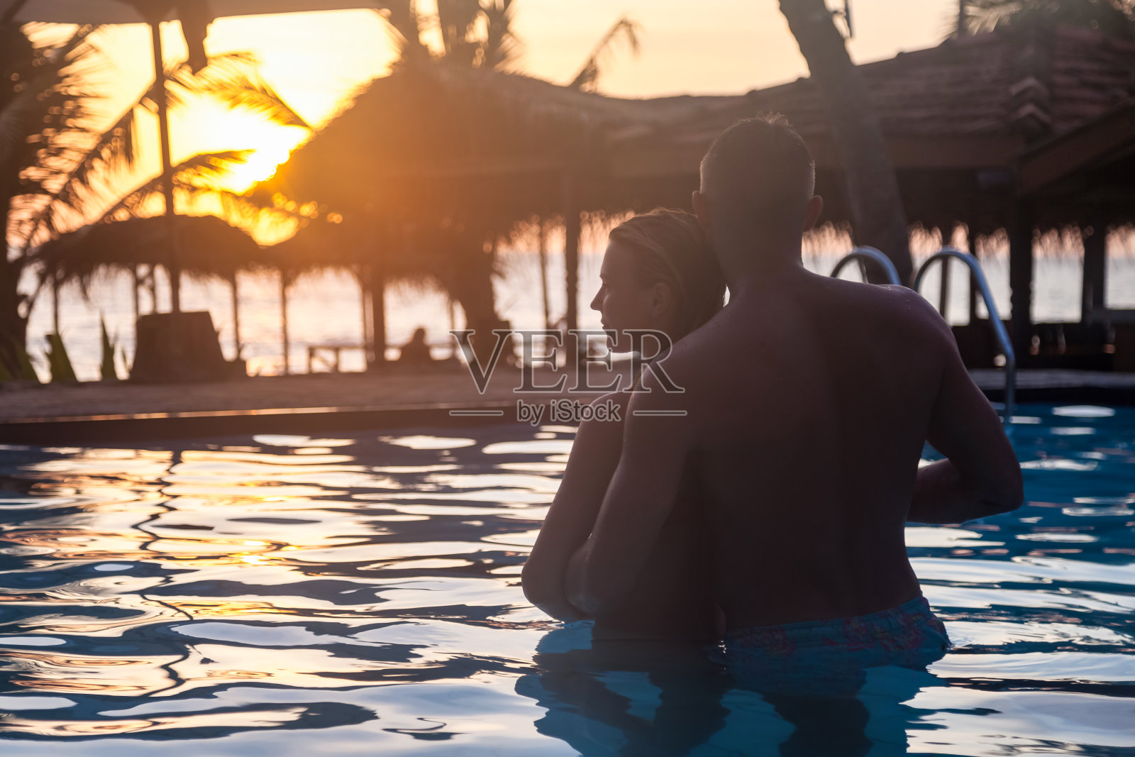 可爱的情侣剪影在游泳池,拥抱和看在日落背景。日落时分,男人和女人在游泳池里休息。夫妇享受蜜月。旅游度假的概念。本空间照片摄影图片