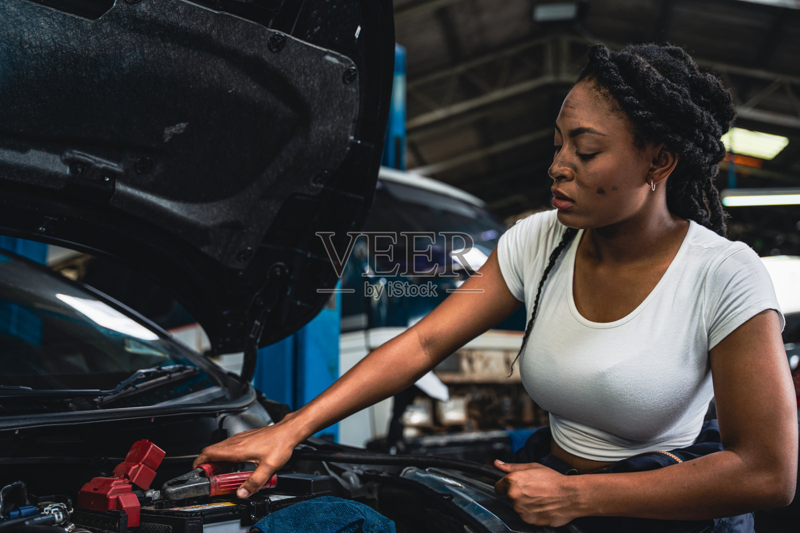 戴着手套的女机械师在车前检查汽车电池。照片摄影图片