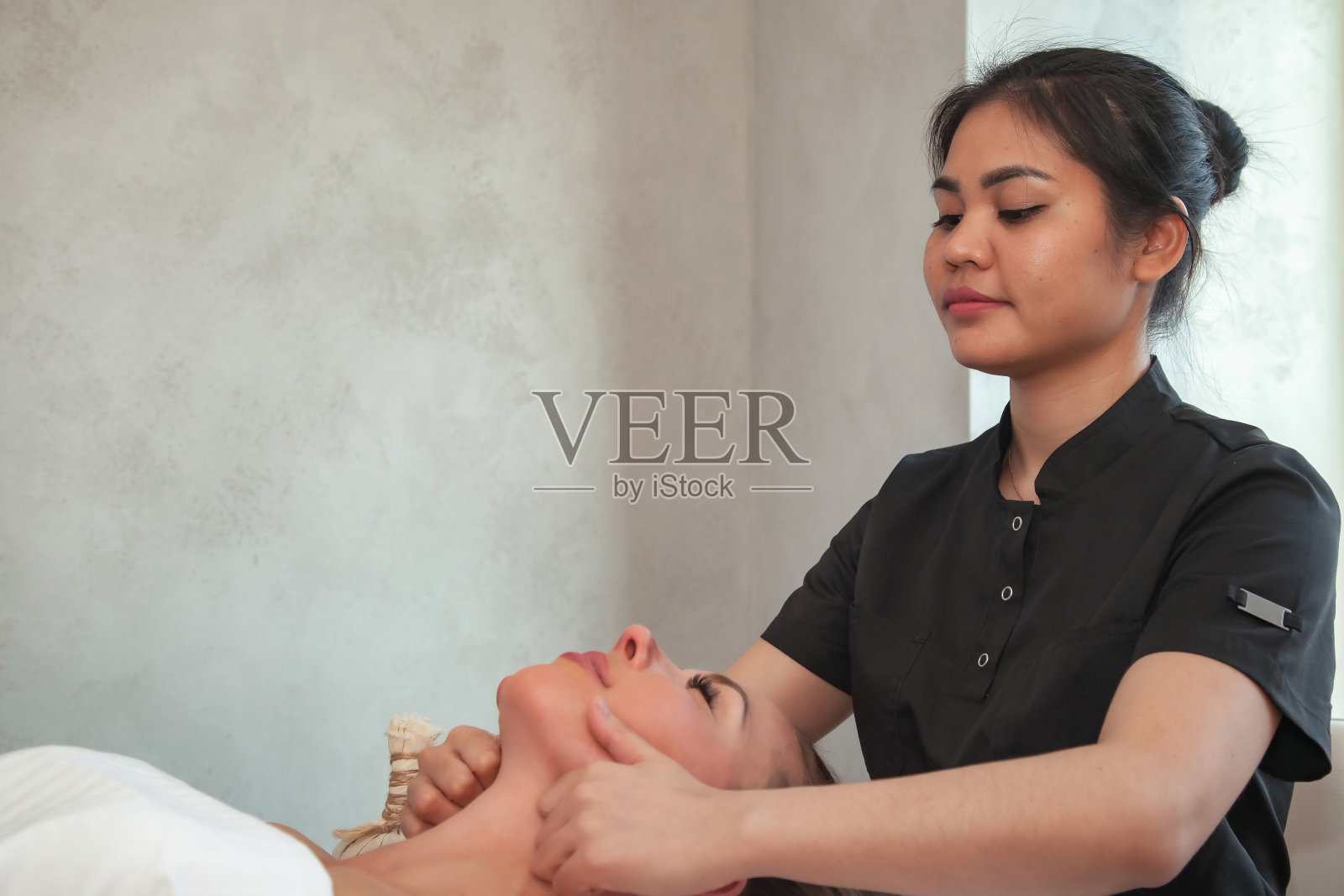 面部按摩妇女在水疗沙龙。按摩师为女性做面部按摩。在专业按摩师手中进行感官健康的按摩。保健和美的概念。本空间照片摄影图片