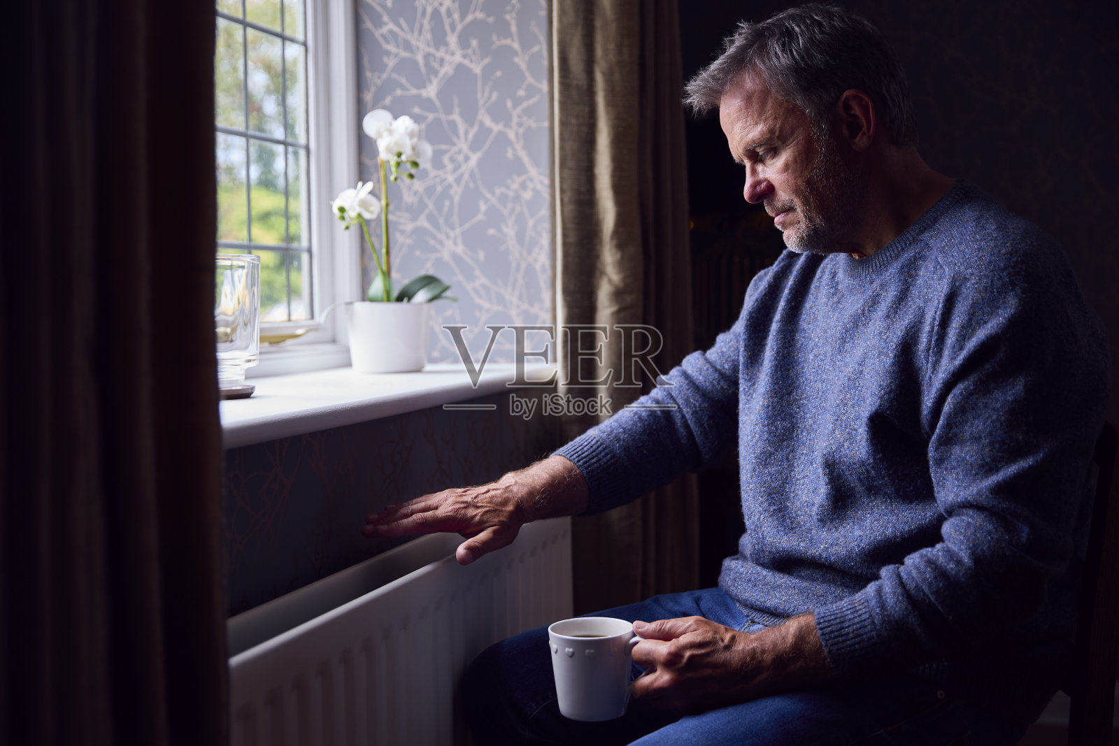 在能源危机期间,一个成熟的男人试图在家里用暖气片取暖照片摄影图片