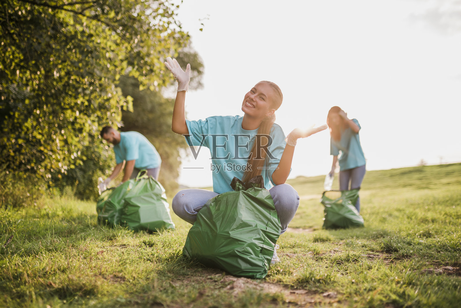 志愿者在公园收集垃圾。一群志愿者站着工作和享受。一群环保主义者在公园里。他们穿着蓝色的t恤。照片摄影图片