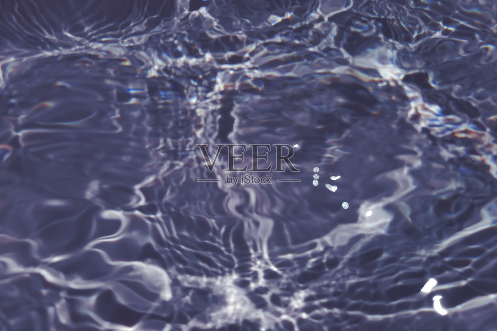 离焦模糊透明蓝色清澈平静的水面纹理与飞溅和气泡。新潮抽象的自然背景。阳光下的水波与复制空间。蓝色水彩闪亮的照片摄影图片