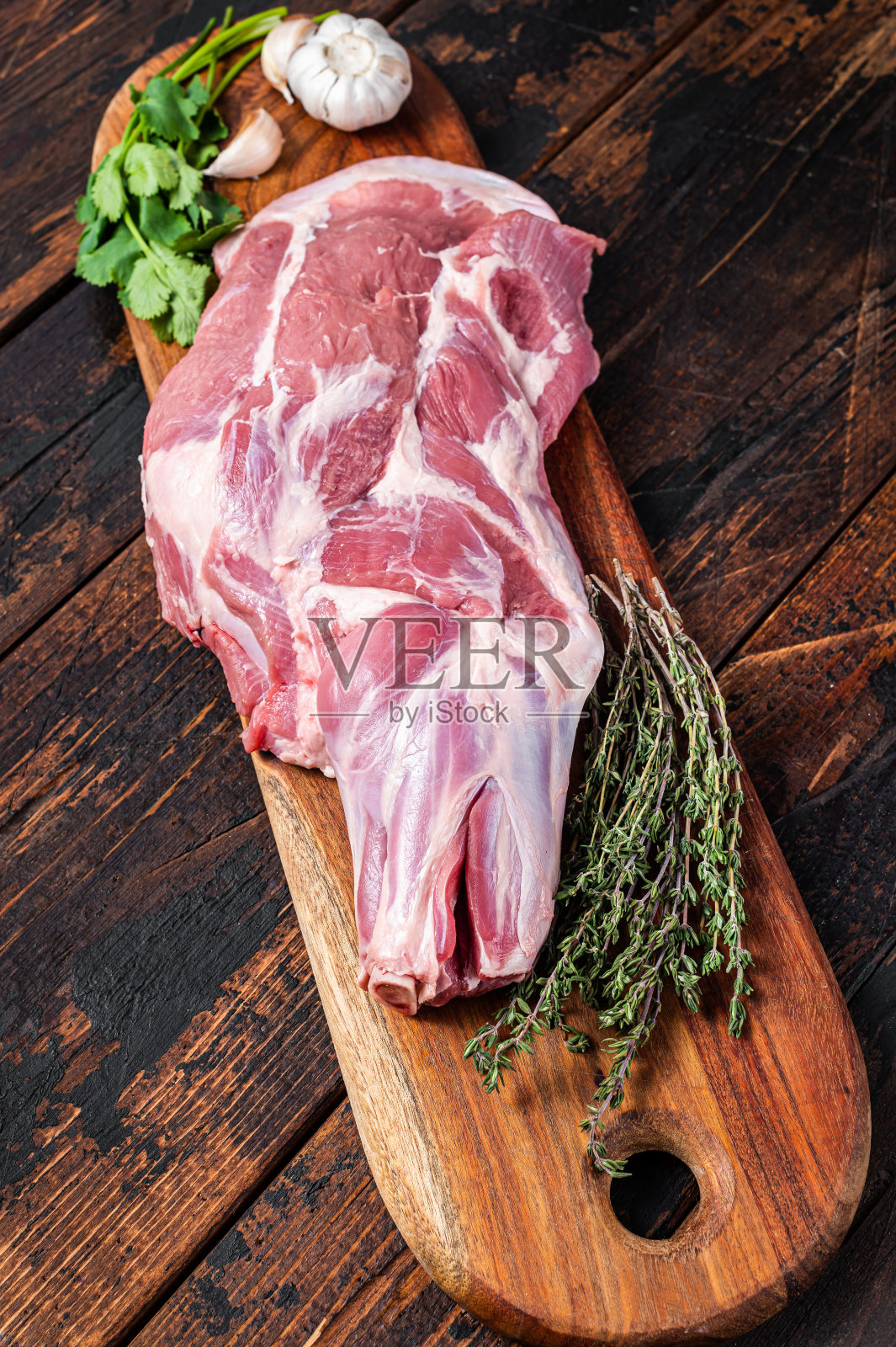 生羊全肩,鲜腿肉放在木板上,配上香料。木制背景。俯视图照片摄影图片