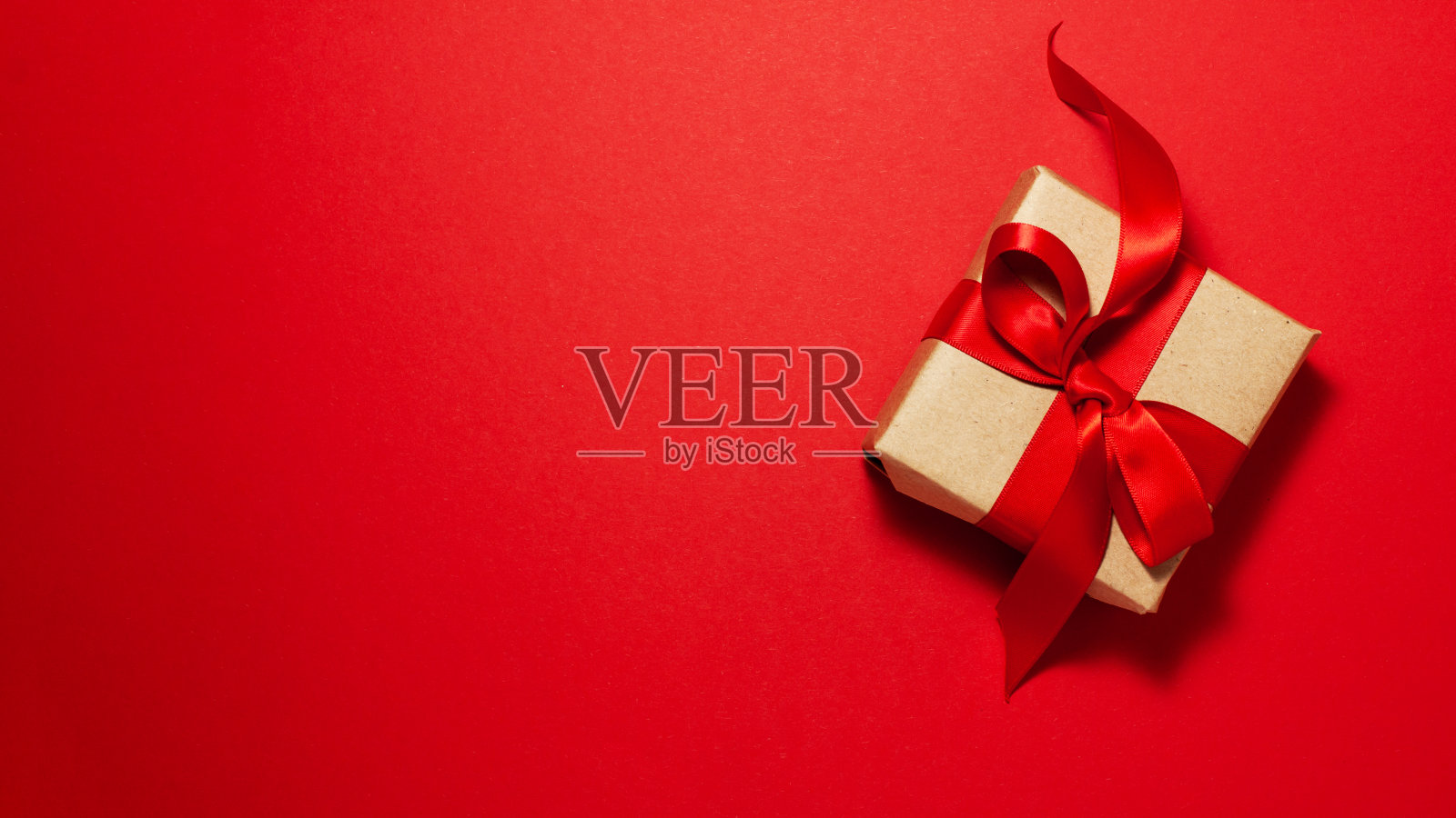 棕色纸礼盒与红色缎带蝴蝶结在红色背景上与右侧的复制空间。平铺情人节爸爸妈妈节和礼物概念照片摄影图片