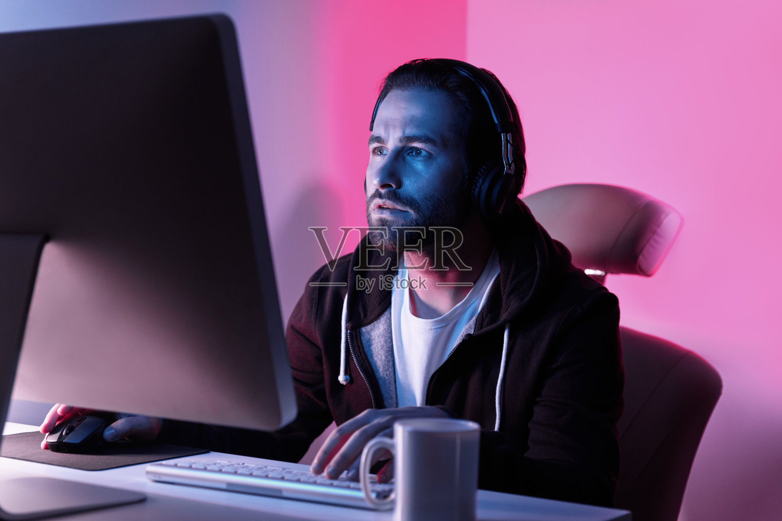 专注的年轻人看着电脑显示器,坐在五颜六色的背景照片摄影图片