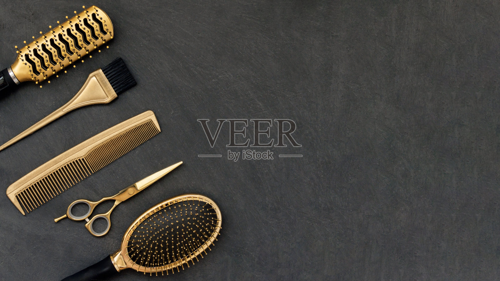 在灰色混凝土背景上的金色美发工具。发廊配件、梳子、剪刀在角落和复制空间照片摄影图片
