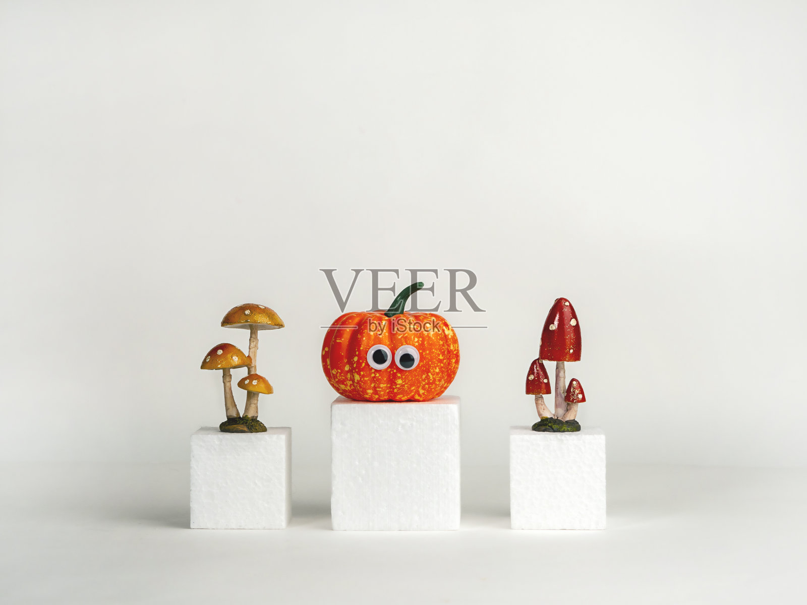 白色立方体上有眼睛和蘑菇的有趣南瓜。万圣节的概念。有创意的想法。”照片摄影图片