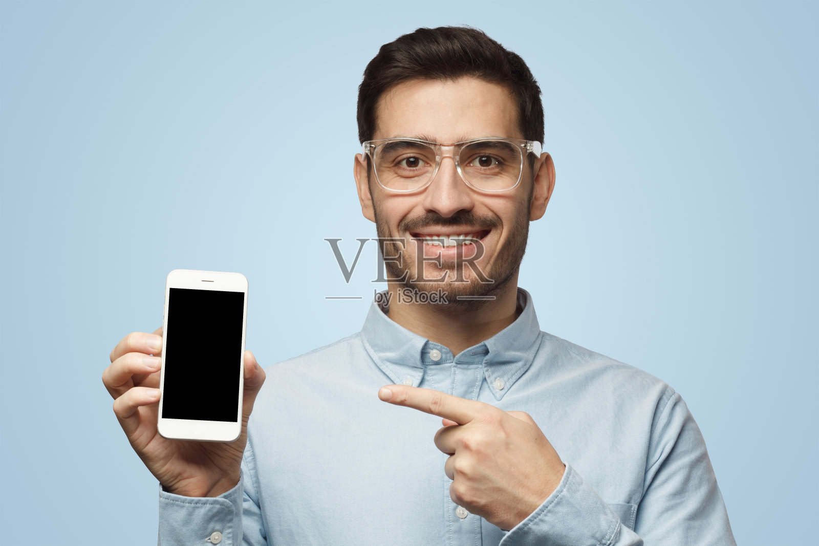 穿着蓝色背景衬衫的男子展示手机,手指指向黑色的复制空间屏幕照片摄影图片