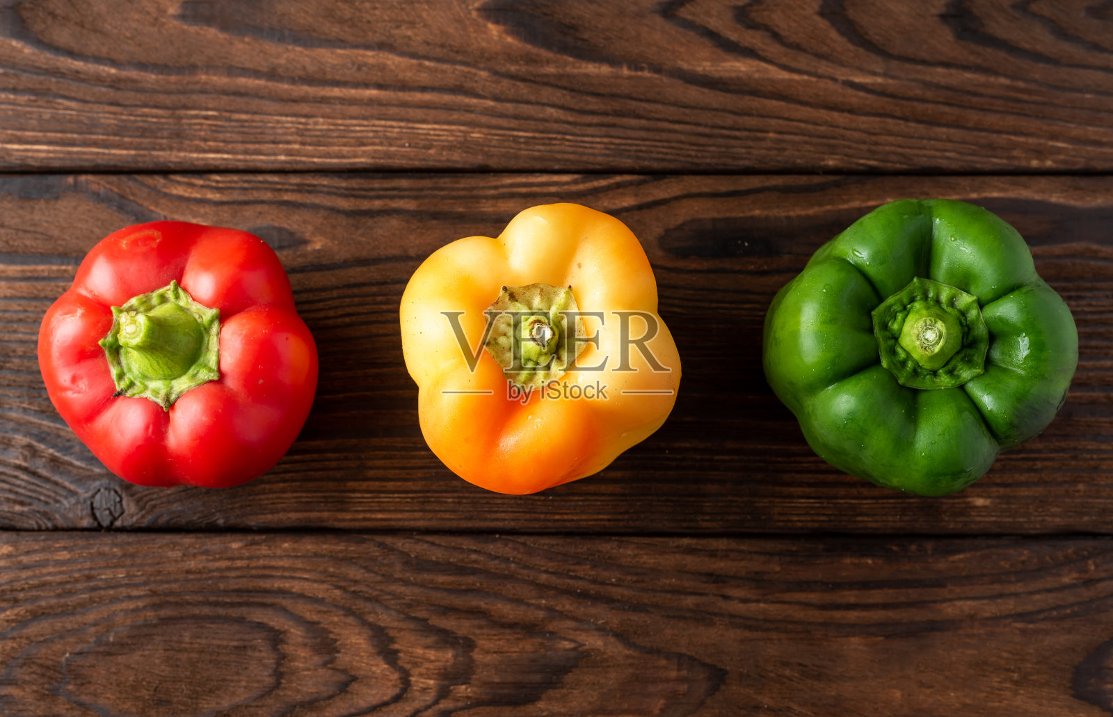 三种不同颜色的辣椒放在木制背景上照片摄影图片