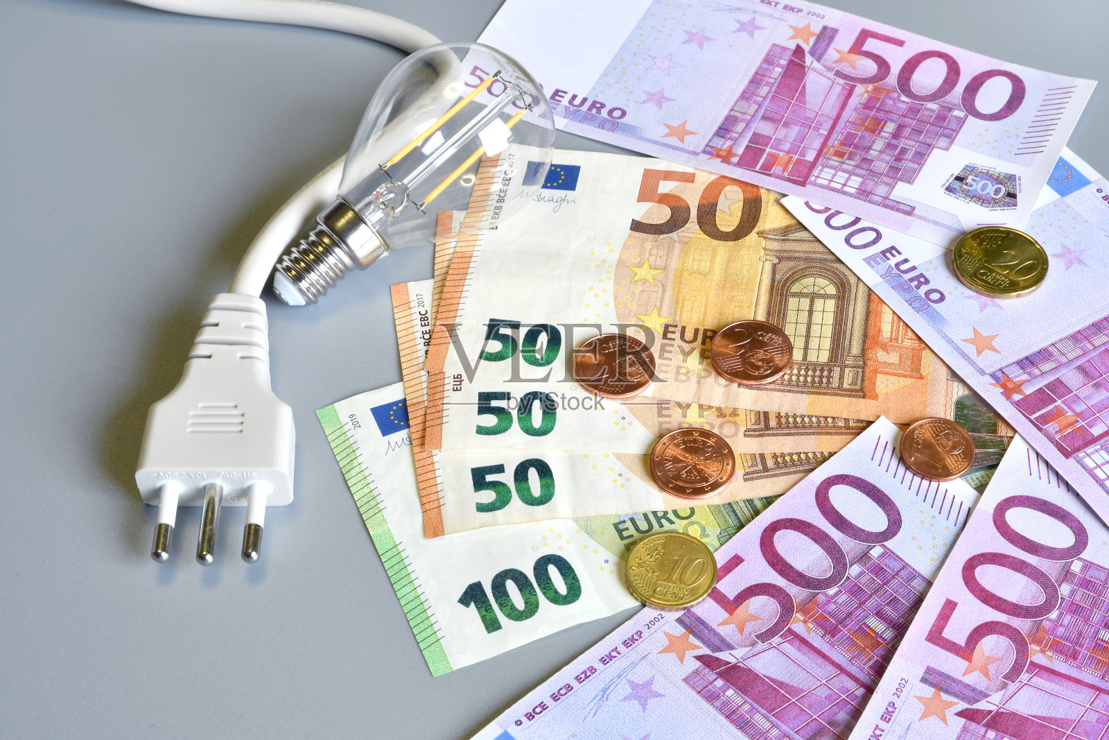 电气插头,欧元纸币和分与灯泡在灰色背景。电力成本增加的概念。昂贵的能源账单和上涨的电价。照片摄影图片