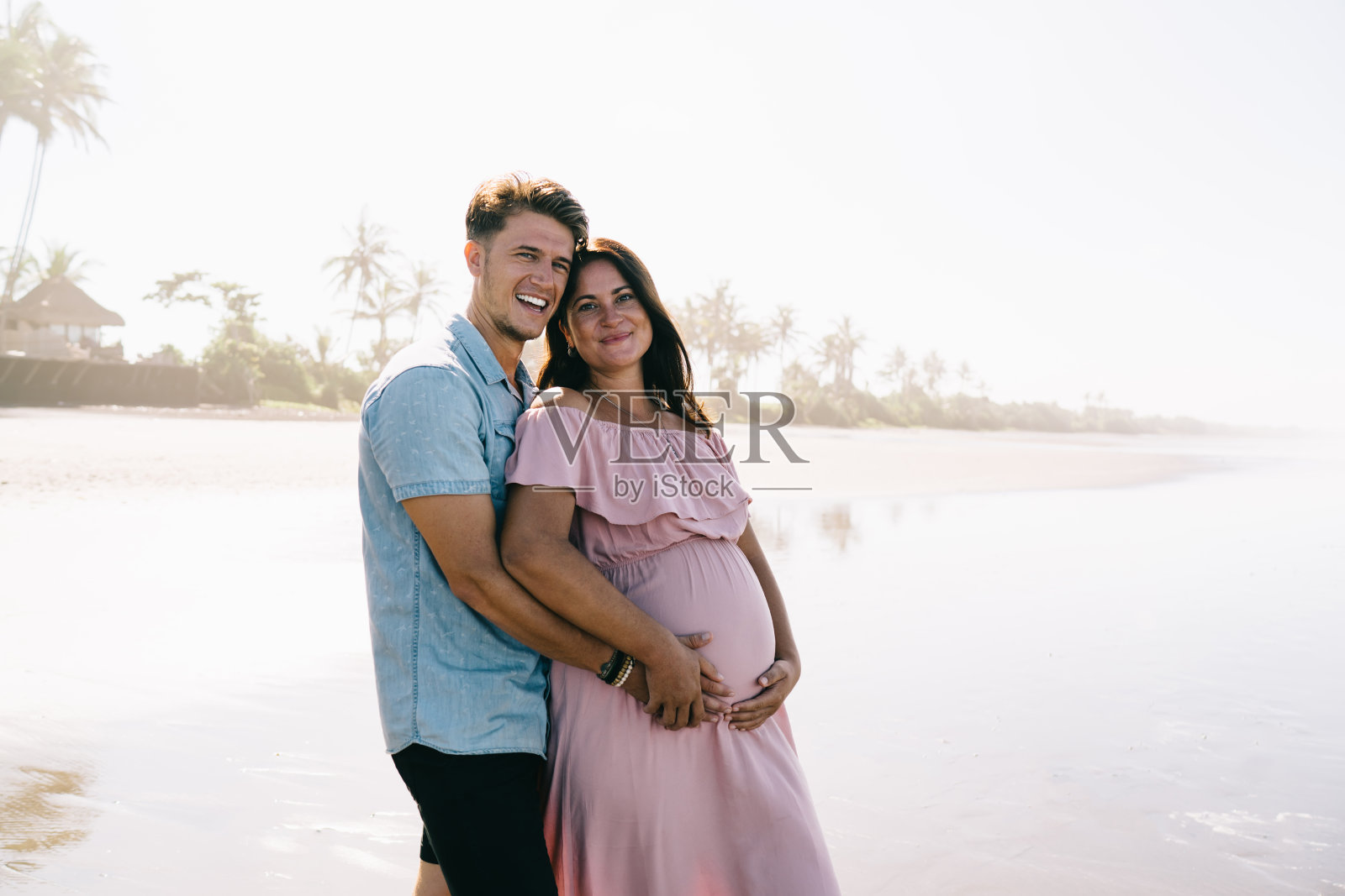 阳光明媚的日子,一对微笑的情侣在海边拥抱照片摄影图片