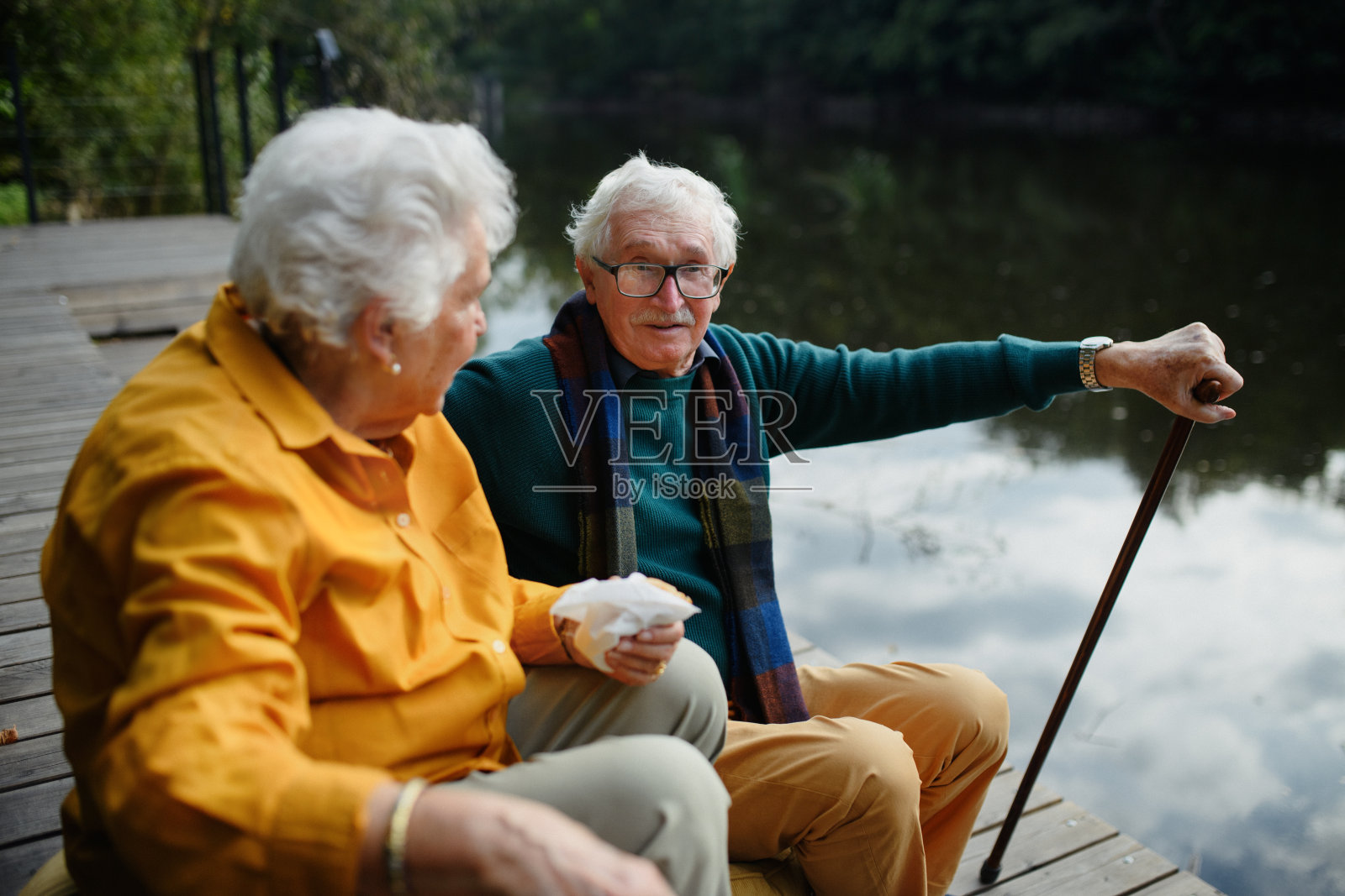 快乐的老夫妇穿着秋装,散步后在湖边休息。照片摄影图片