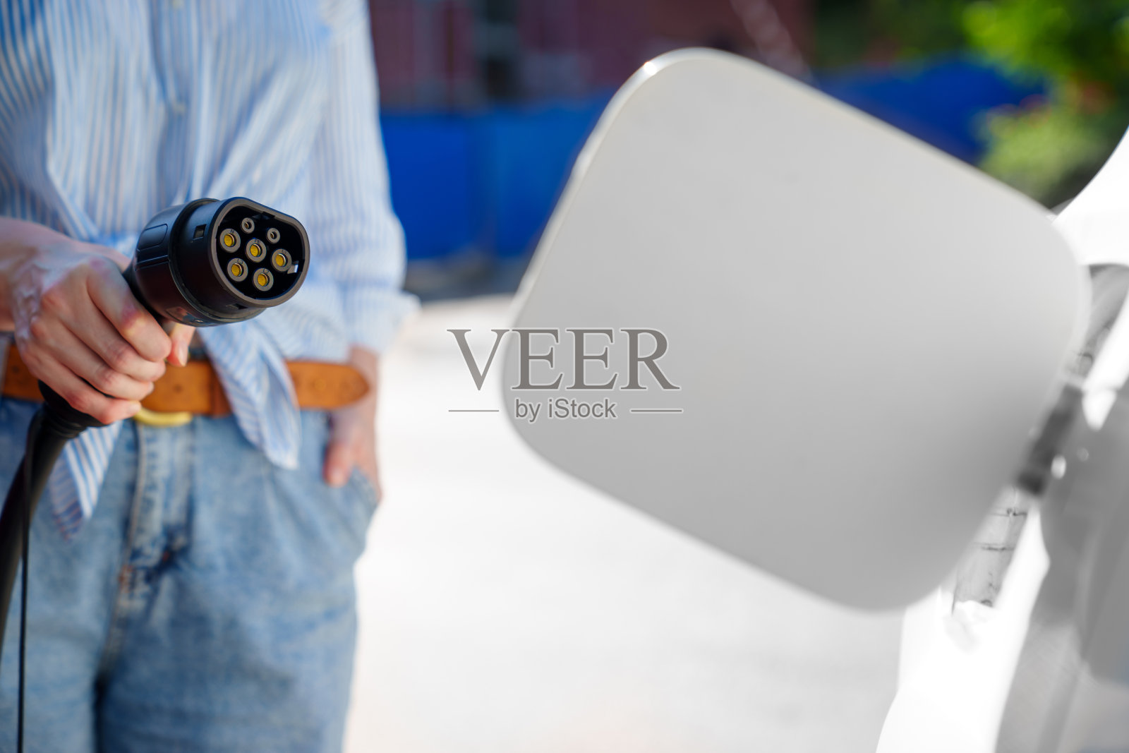 在插座上为电动车充电的女人的手。照片摄影图片