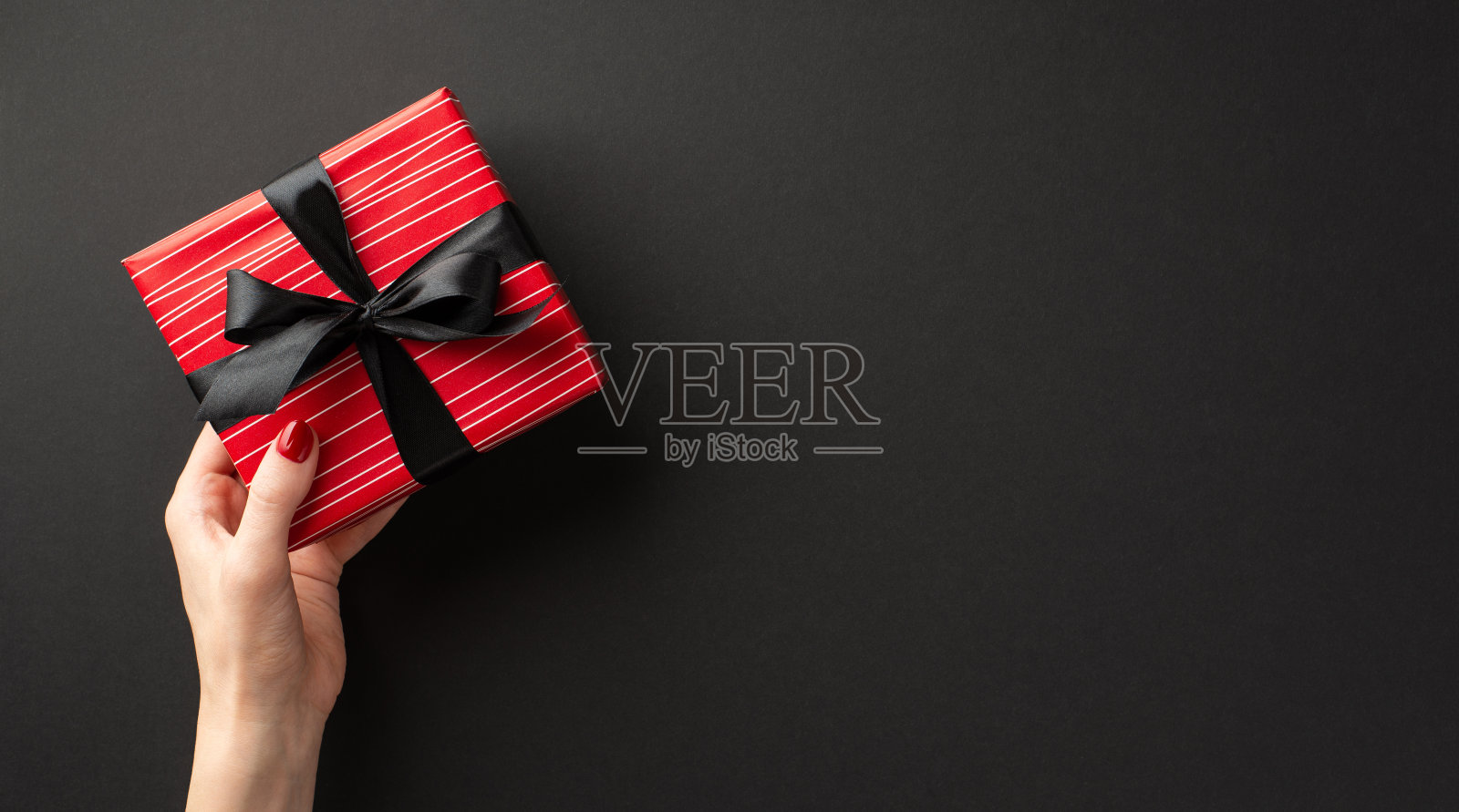 “黑色星期五”的概念。第一人称俯视图照片的女孩的手给红色礼盒与缎带蝴蝶结孤立的黑色背景与空白照片摄影图片