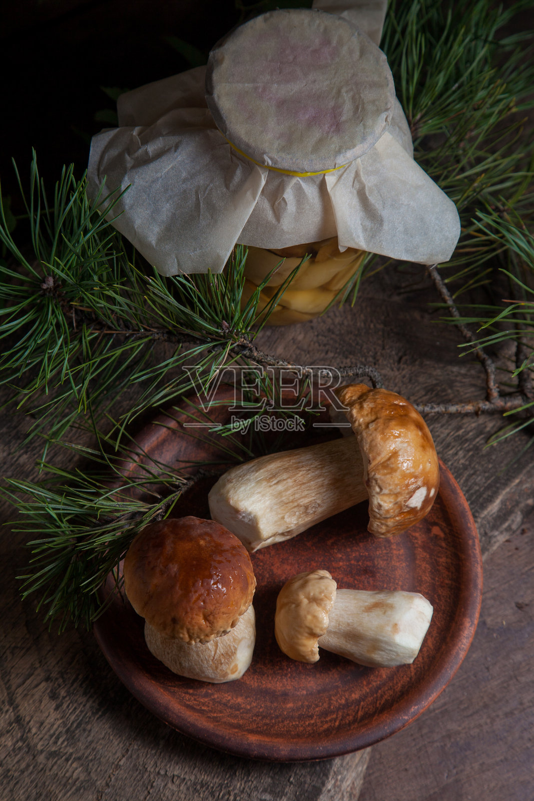 陶制盘子与三个牛肝菌蘑菇通常被称为Boletus Edulis和玻璃罐罐头蘑菇在古老的木制背景。照片摄影图片