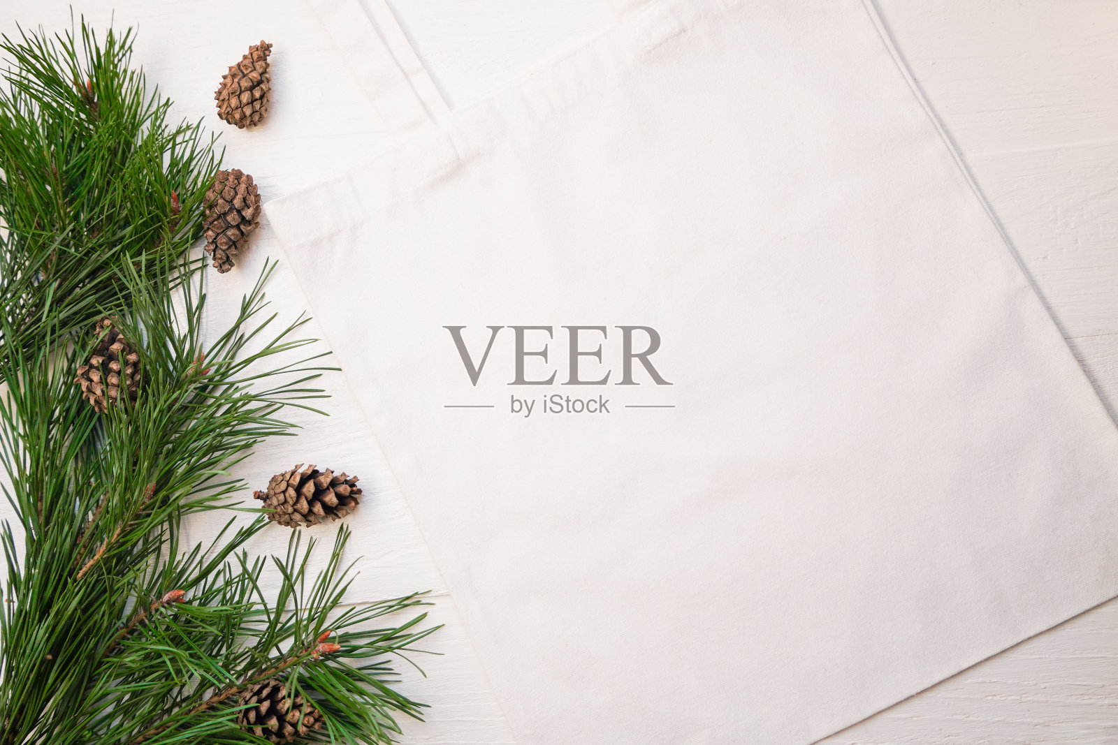 实物环保米色或白色彩色帆布棉布袋松枝和球果在白色木制背景。购物袋模型空白模板。可重复使用的杂货袋和购物袋。冬天,圣诞节和新年的背景概念照片摄影图片