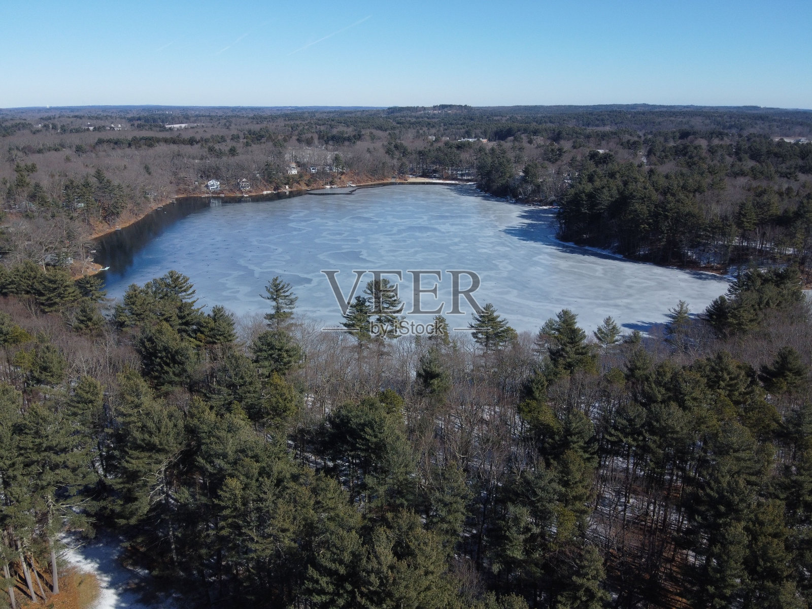 空中拍摄的一个被松树包围的小冰冻湖在白天照片摄影图片