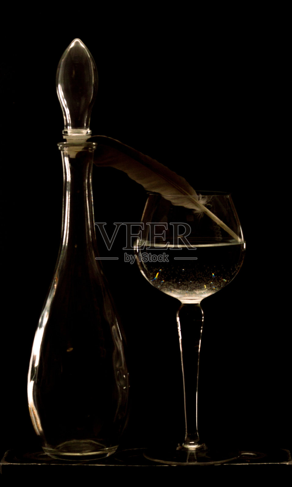 垂直镜头的一个酒杯与羽毛在它和一个玻璃瓶在一边照片摄影图片