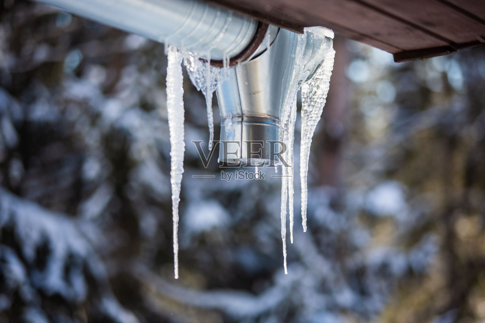 在模糊的背景下,冰柱悬挂在屋顶上的特写镜头照片摄影图片