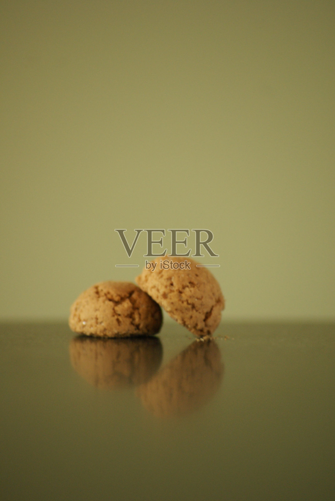 在橄榄绿背景的桌子上,垂直拍摄了两颗苦杏。照片摄影图片