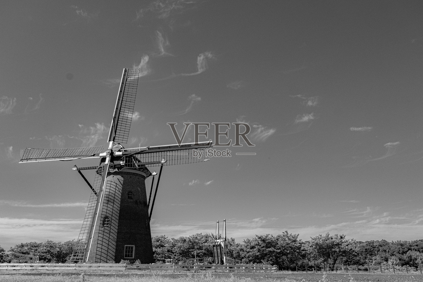 田野上风车的灰度图,背景是树木和天空。照片摄影图片