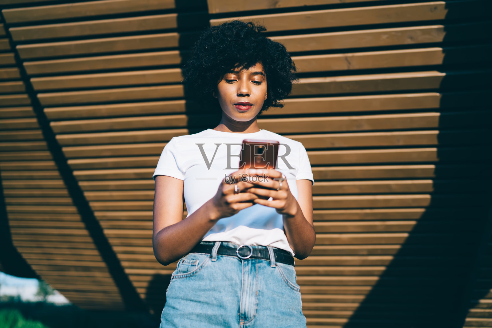 年轻的非洲裔美国人在木制建筑附近用智能手机发短信照片摄影图片