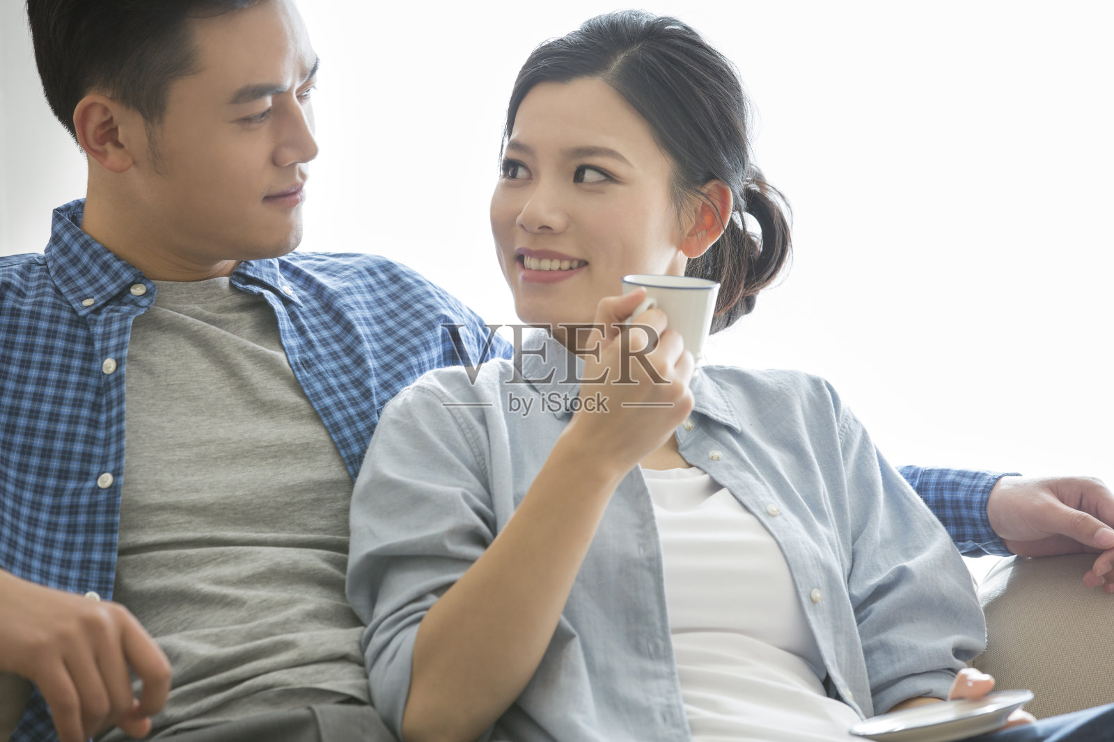 年轻的夫妇在沙发上休息,丈夫为他月经来的妻子准备热饮-库存照片照片摄影图片