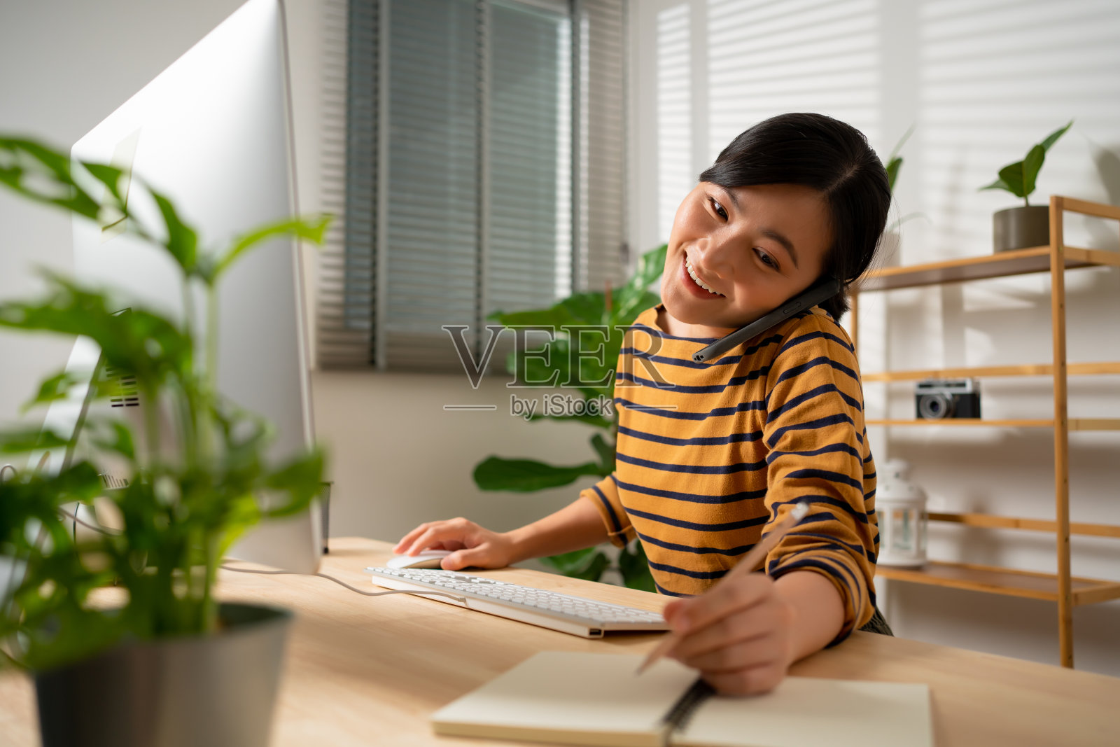 亚洲女性喜欢在家办公,一边打电话一边工作。照片摄影图片