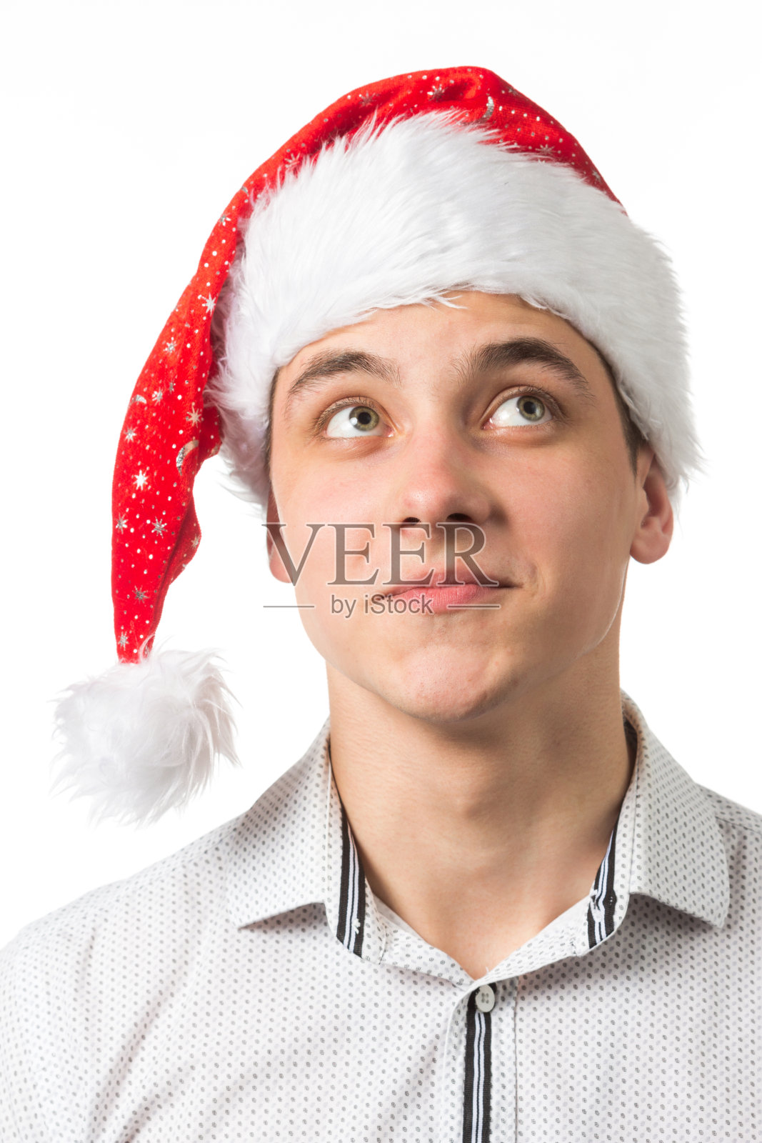 年轻英俊的男子戴着圣诞老人的帽子在白色的背景惊讶,显示和指向的东西是在她的手上照片摄影图片